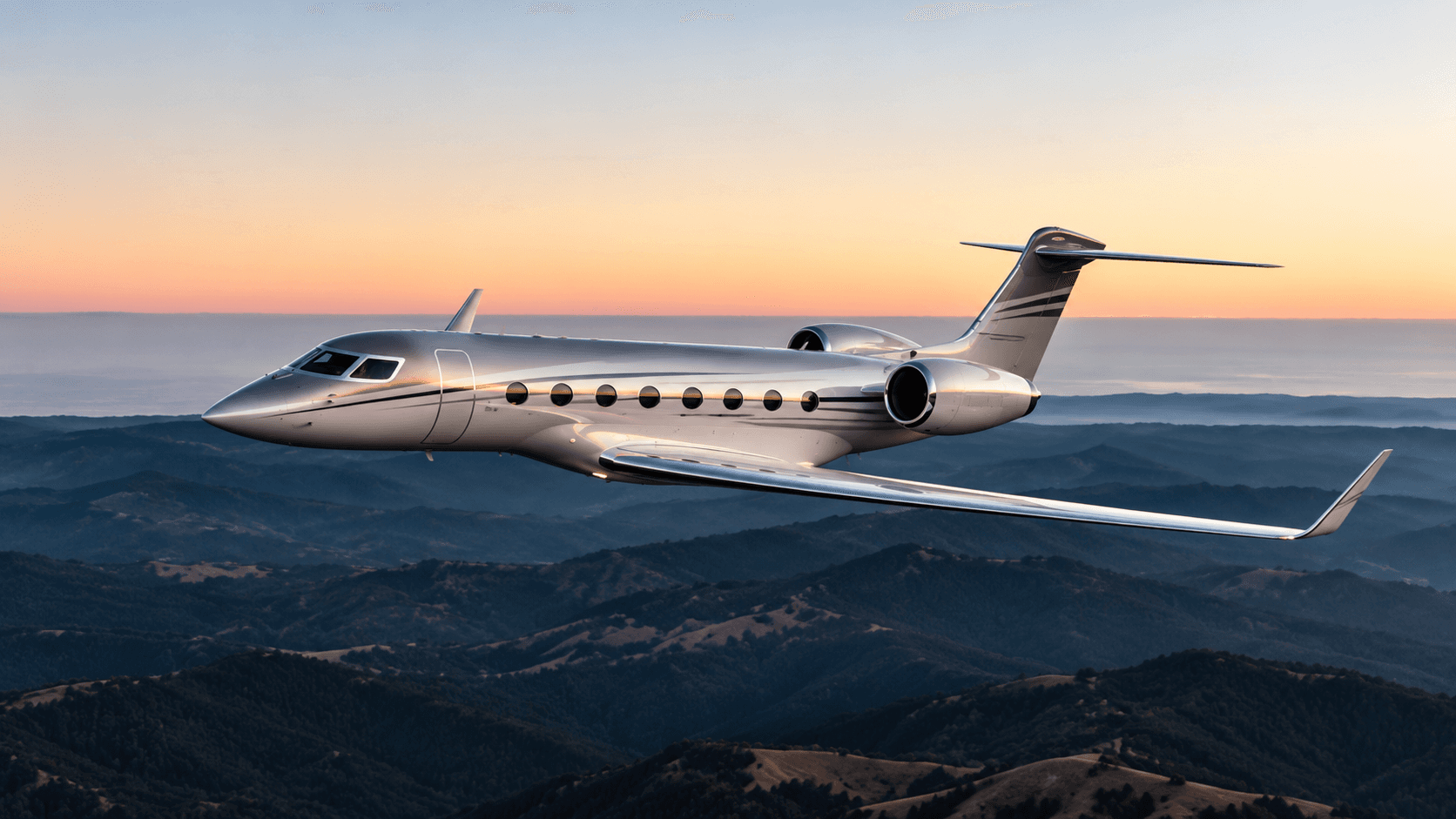Silver business jet above mountain ridges at sunset